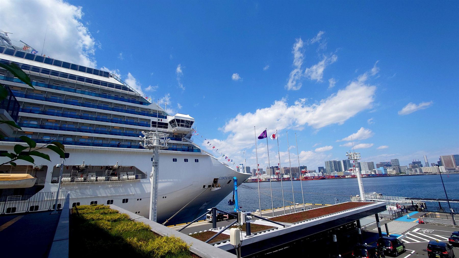 A cruise ship docked at a cruise terminal in Japan, with a city skyline across the bay
