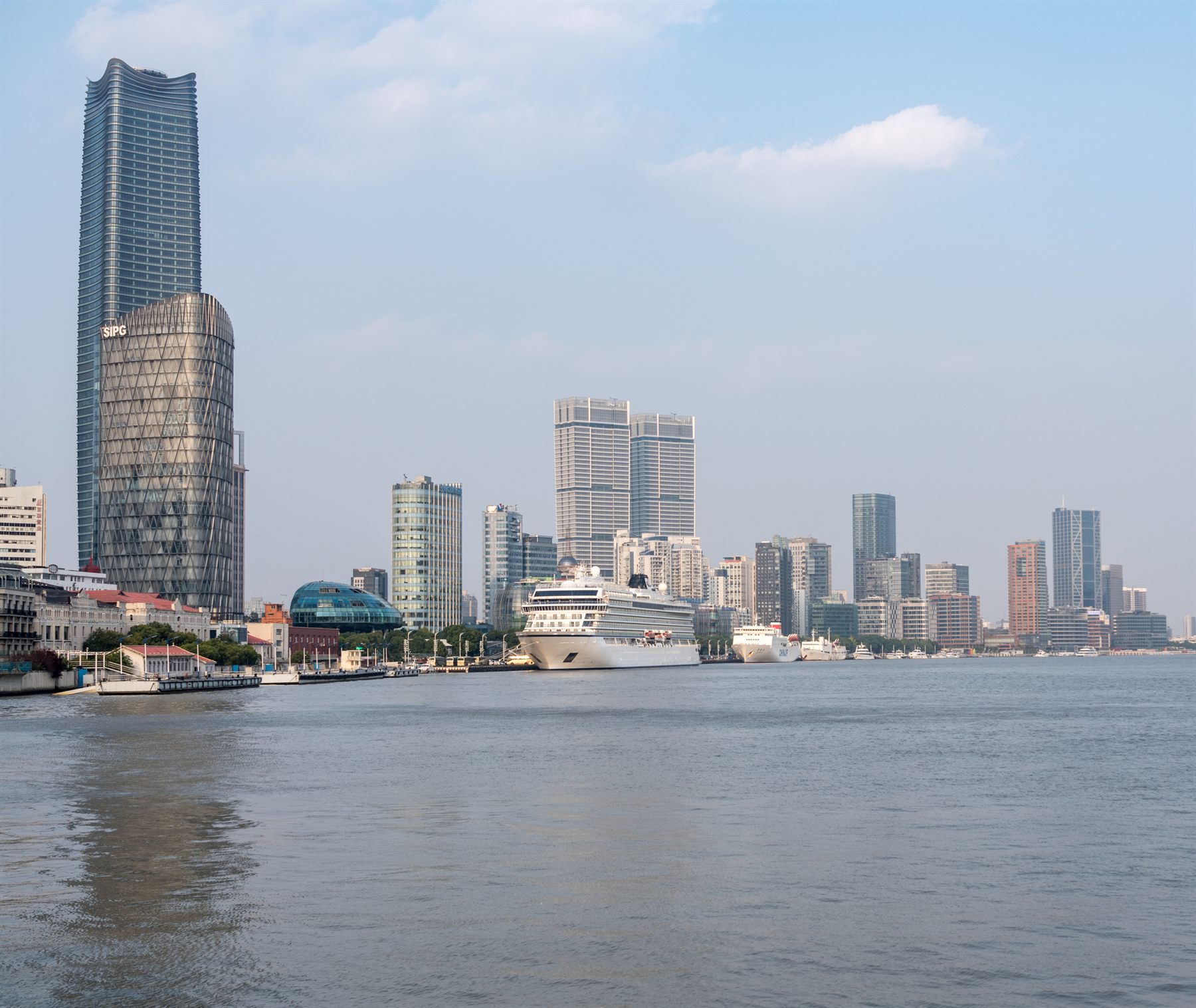 A cruise ship docked along a high-rise waterfront skyline in an Asian port city